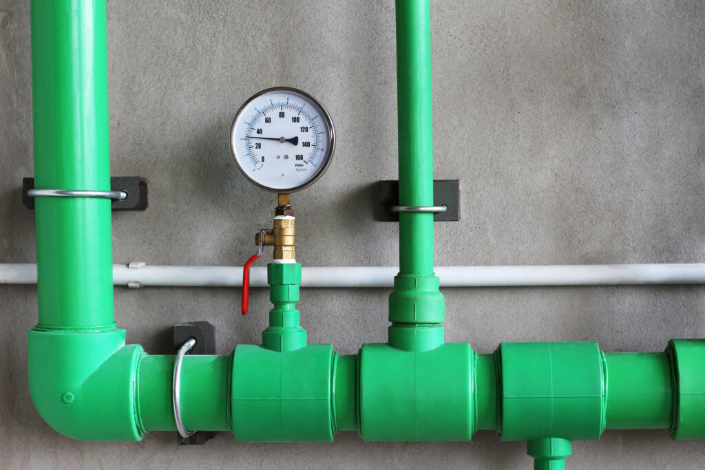 Water pressure gauge with valve in pipe on concrete wall background.