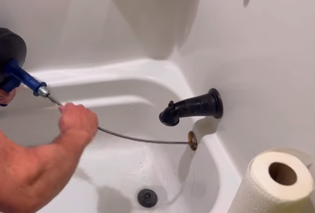 Plumber feeding a drain cable through the overflow opening of a clogged bathtub drain