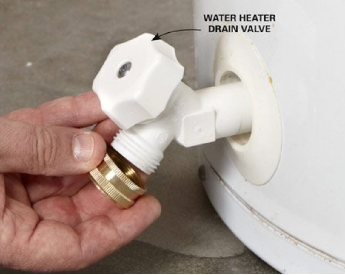 Hand on the drain valve at the base of a residential water heater, the fitting used when isolating a tank during an emergency plumbing call in Wake Forest, NC