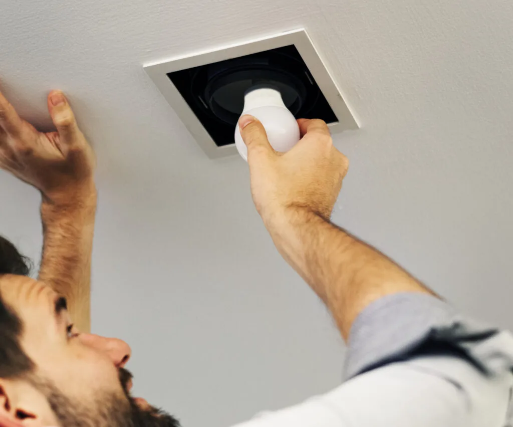 Man reaching up to screw an LED bulb into a recessed square ceiling fixture.