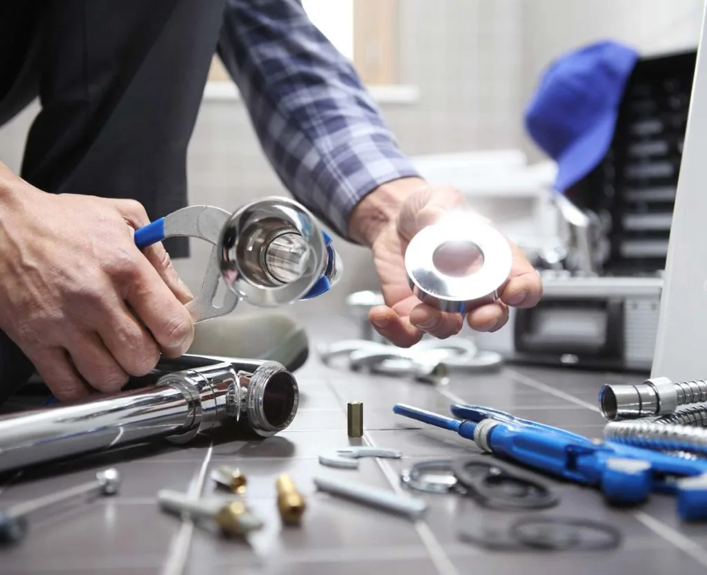 Close-up of a plumber's hands assembling a chrome faucet with pliers and fittings.